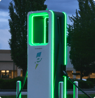 A group of Electrify America fast chargers glowing green at night.