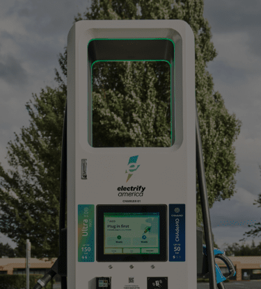 A group of Electrify America fast chargers in a tree-lined shopping center.