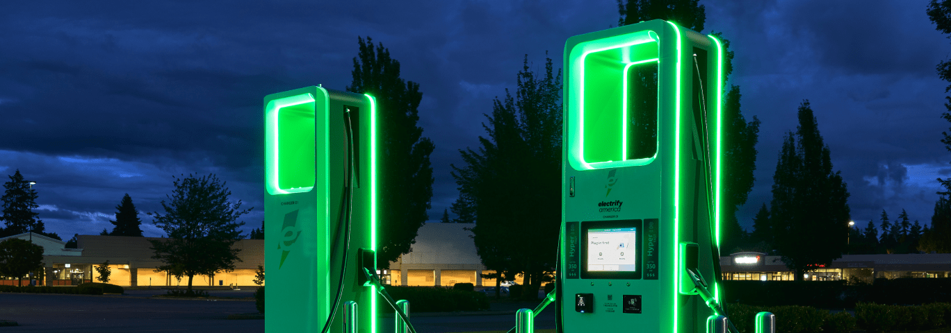Two Electrify America charging stations glowing green at night