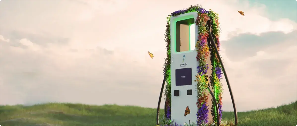 Electrify America charger in a field at sunset, wrapped in colorful flowers with three butterflies flying nearby.